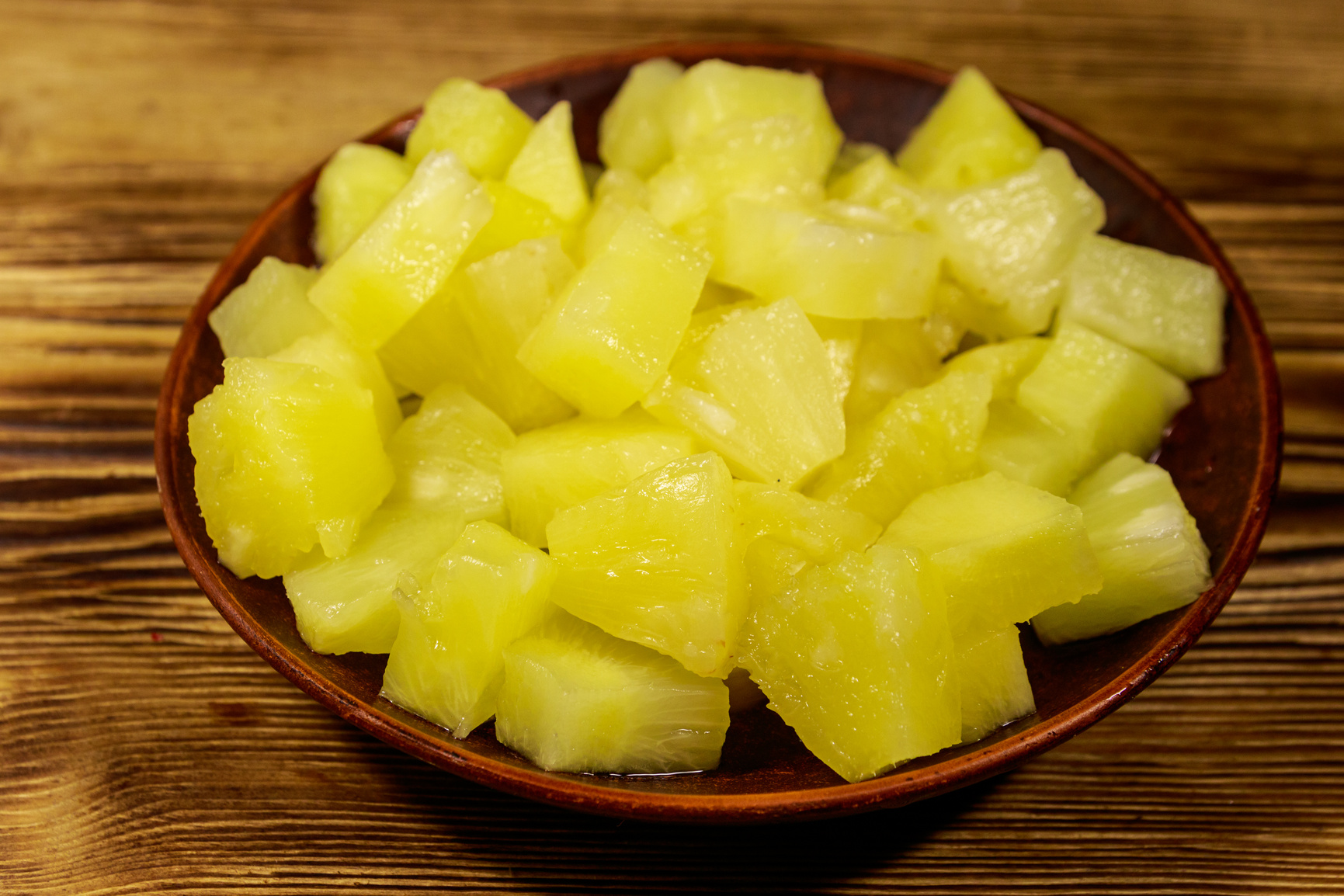 Canned pineapple pieces in ceramic plate on wooden table